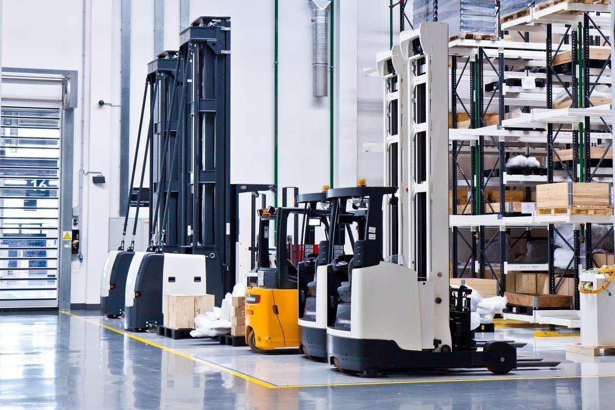 Electric reach trucks and a stand-up forklift parked in a warehouse &mdash; the equipment that runs on polyurethane load wheels.
