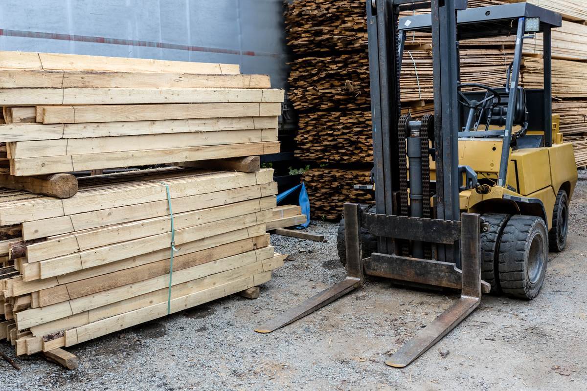 Weathered yellow pneumatic-tire forklift parked between stacks of cut lumber in a sawmill yard