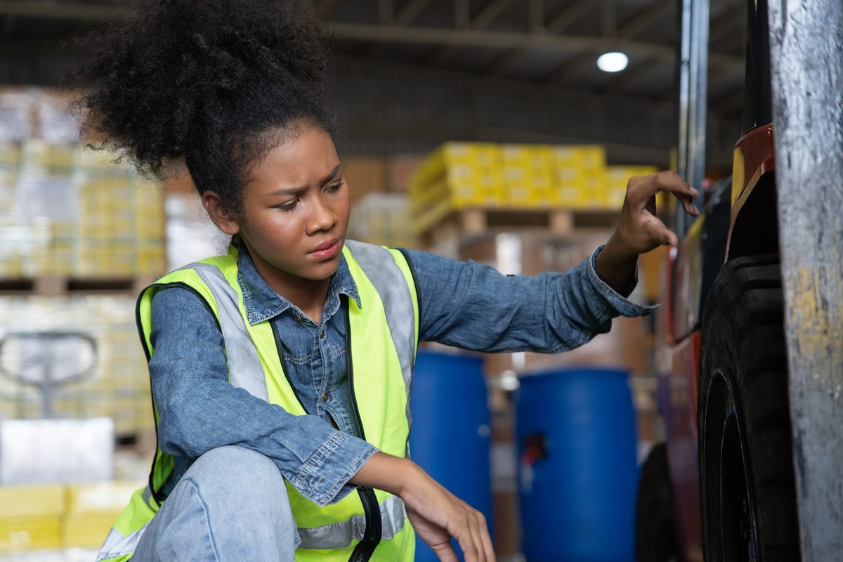 Warehouse worker in a hi-vis vest inspecting a forklift tire for wear