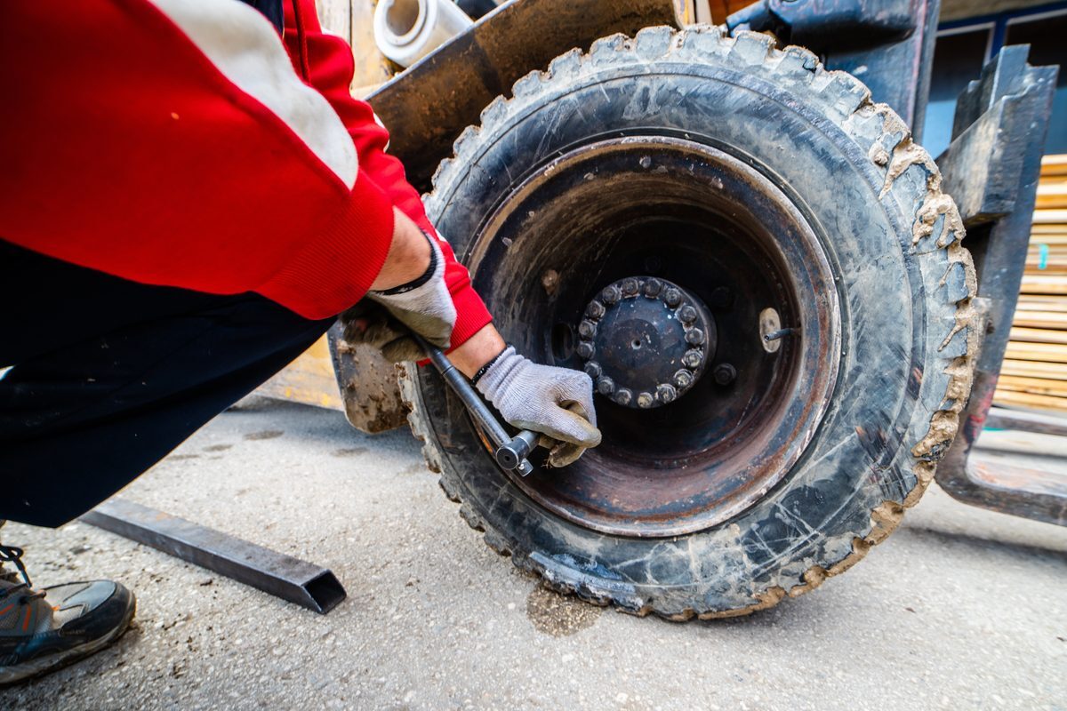 Worn, cracked pneumatic forklift tire being removed for replacement