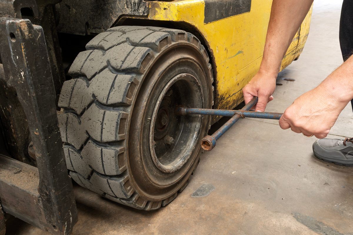 Technician replacing a worn forklift tire with a lug wrench