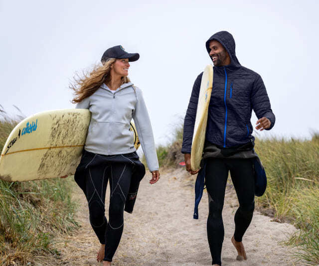 Man and woman walking on beach wearing Cutter & Buck jackets and layers.