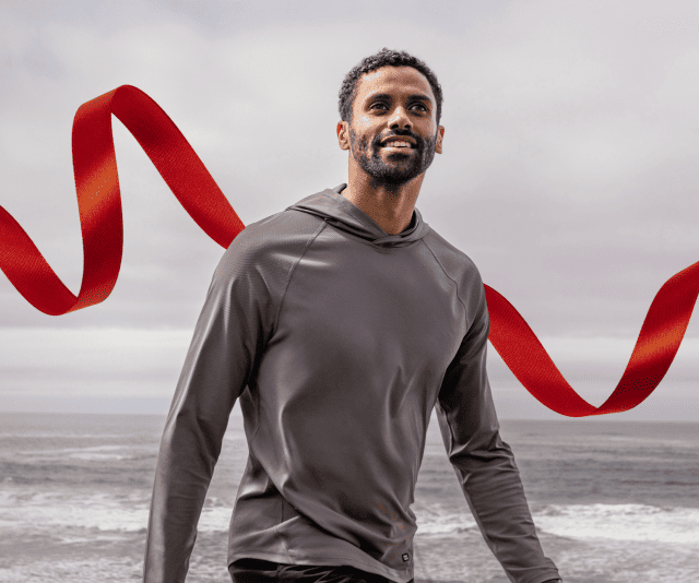 Man wearing a gray hooded sweatshirt, standing on a coastal vista.