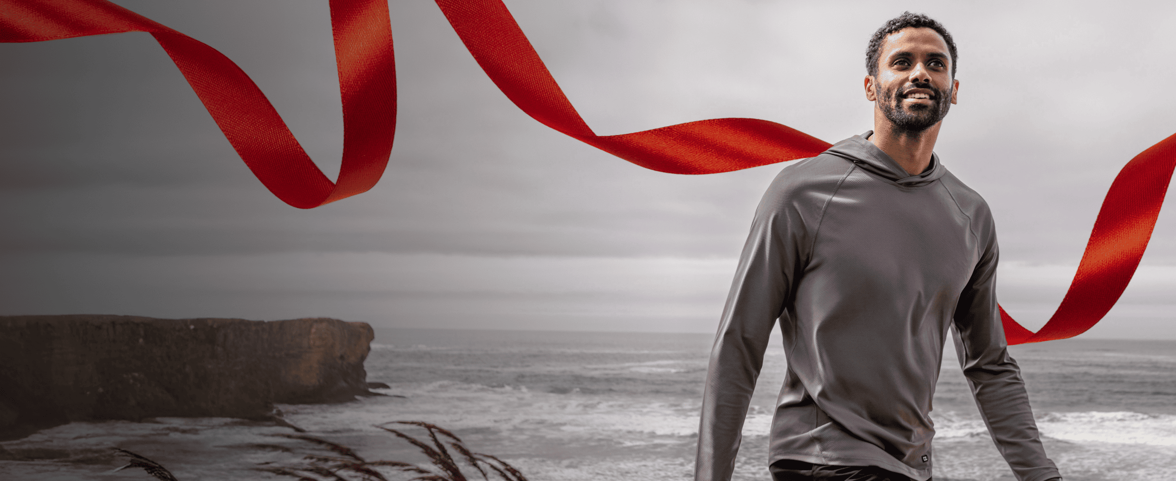 Man wearing a gray hooded sweatshirt, standing on a coastal vista.