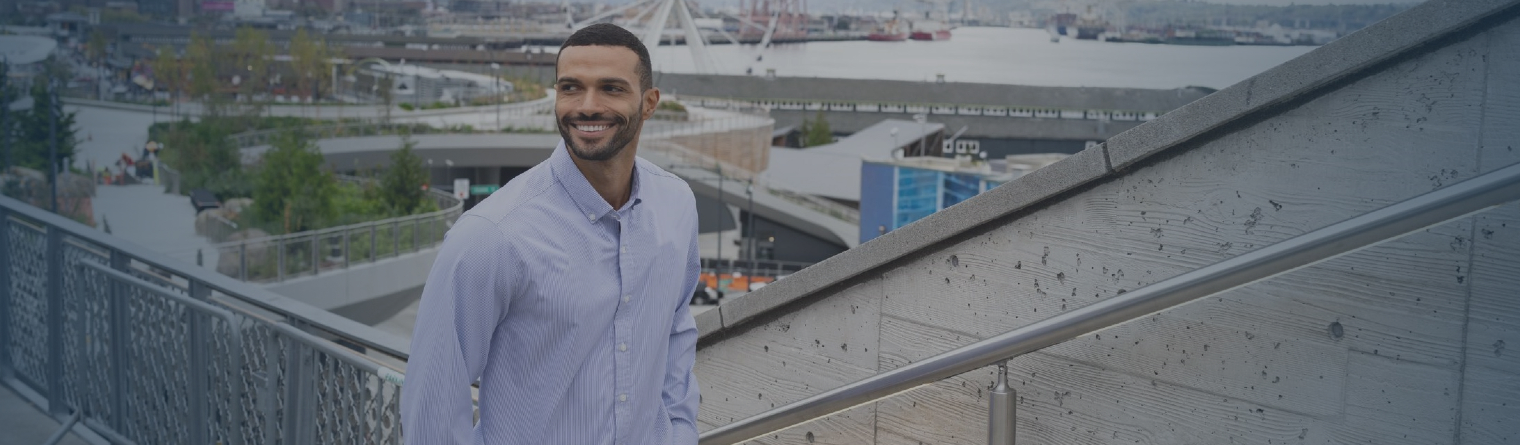 man walking outdoors in Seattle wearing a Cutter & Buck button-down shirt and pants, with the Seattle Great Wheel and waterfront in the background.

