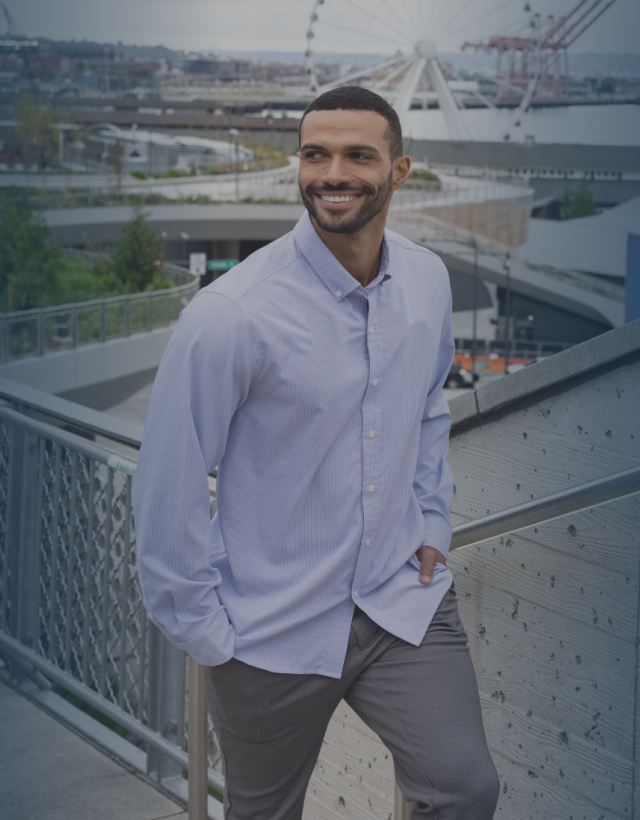 man walking outdoors in Seattle wearing a Cutter & Buck button-down shirt and pants, with the Seattle Great Wheel and waterfront in the background.
