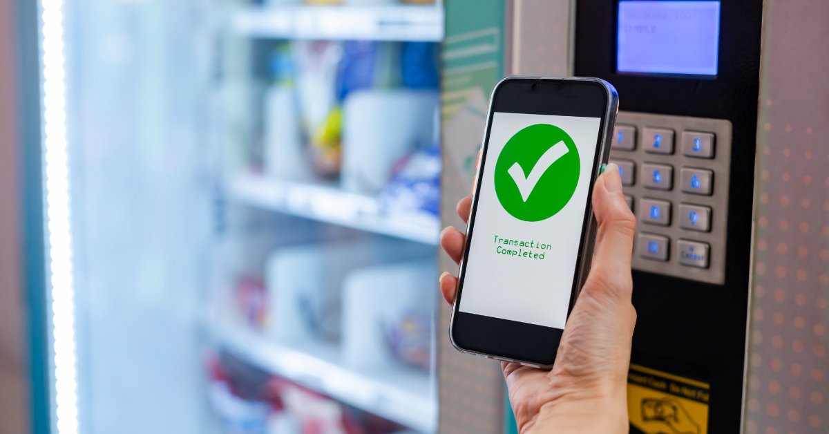 Customer using a smartphone for a cashless payment at a vending machine, illustrating payment compatibility and modern cashless vending technology.