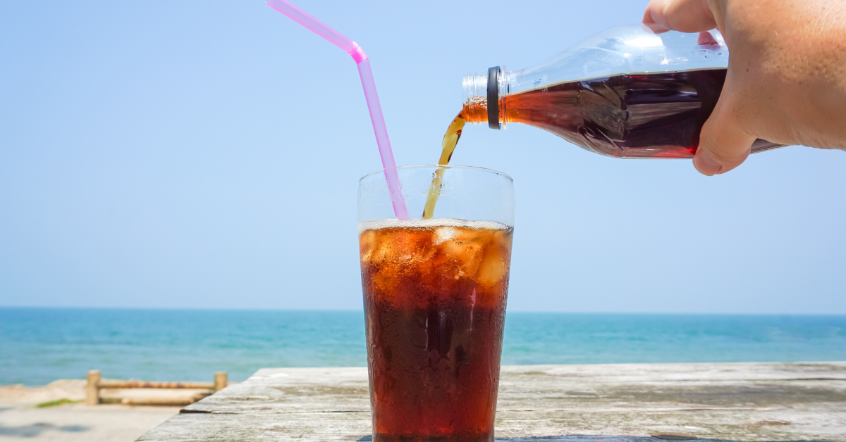 Cold soda being poured into an ice-filled glass near the beach during summer