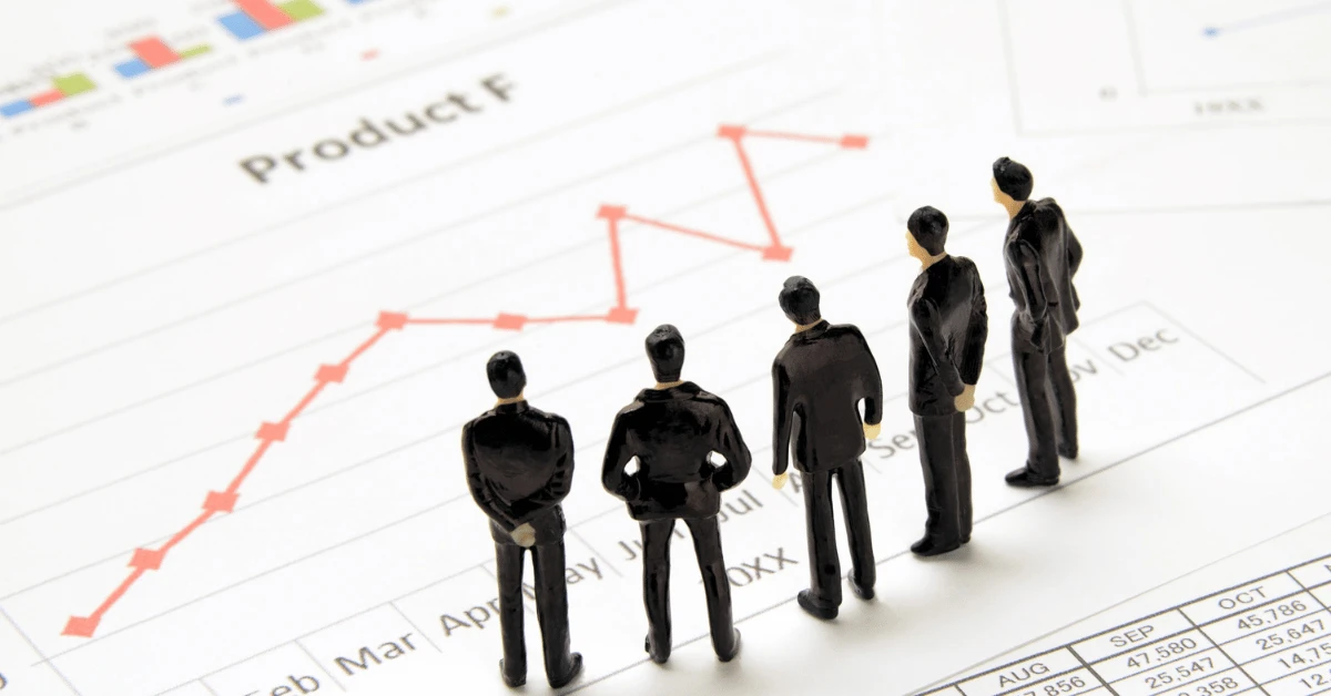 Five miniature business figures standing on a financial chart with an upward-trending red line.