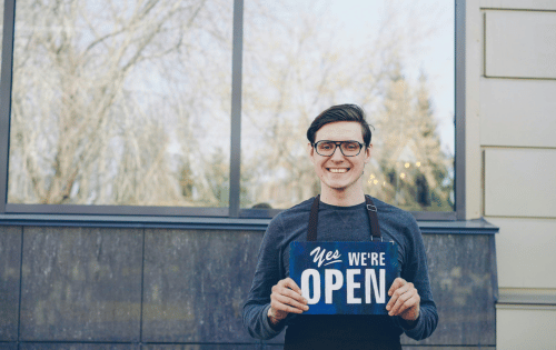 Small business owner holding a we are open sign outside a storefront