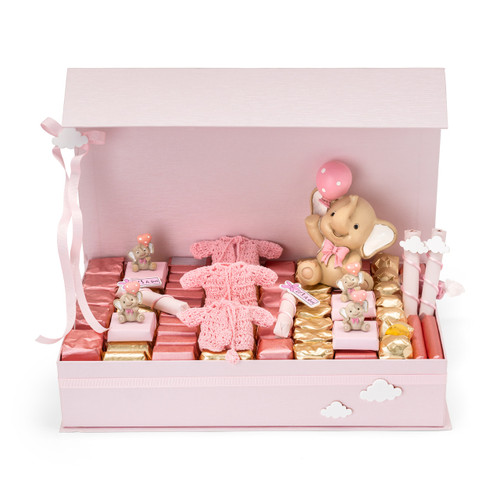 A light pink chocolate gift box featuring a smiling elephant figurine holding a pink balloon, chocolates wrapped in pink and gold papers, crochet-style jacket chocolates, and small elephant figurines holding balloons, accented with acrylic clouds.