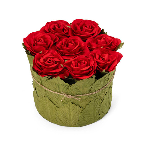 A handmade paper box with a flat lid adorned with red paper roses and green leaf details, containing 1.5 pounds of assorted premium chocolates, including ashta-flavored chocolates with pistachio toppings and chocolates in see-through wrapping.