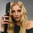 A woman with wavy hair holding the Bio Ionic 10X Styling Iron.