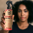 A woman with curly hair holding the 2 Phase Detangler Spray.