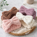 Blush, brown, beige, and purple plush bow spa headbands arranged on a tray