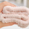 Stacked blush plush spa wristbands held in one hand