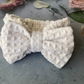Beige waffle-texture bow spa headband on a floral backdrop