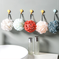 Five floral mesh bath poufs in assorted colors hanging above a sink
