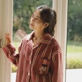Woman wearing rust red striped plush pajamas beside a sunlit window