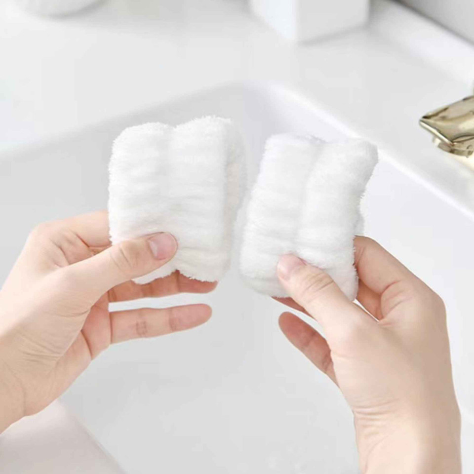 Pair of white plush spa wristbands held above a sink