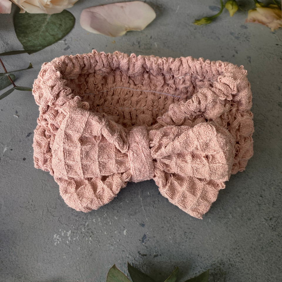 Pink waffle-texture bow spa headband in a floral flat lay