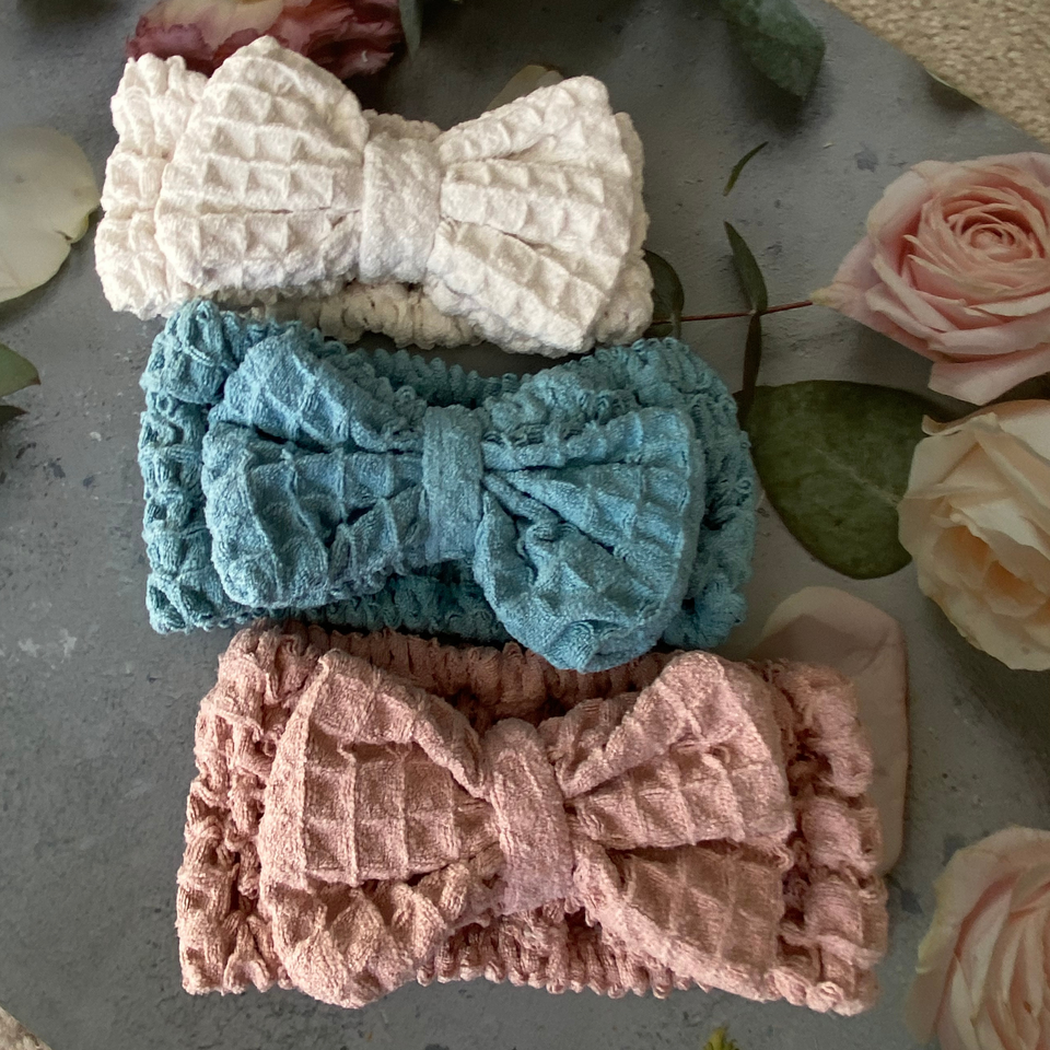 Beige, blue, and pink waffle-texture bow spa headbands in a floral flat lay