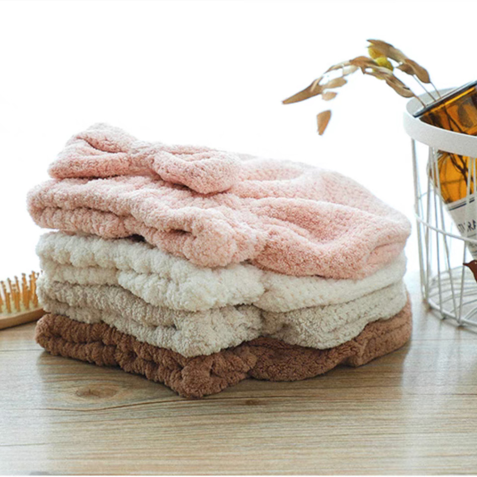 Mauve pink, ivory, and khaki bow hair towels stacked on a table