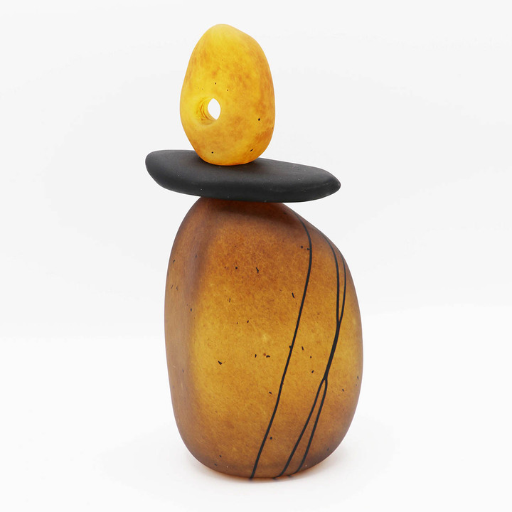 Blown glass cairn sculpture by Melanie Leppla with two glass stones, the top one with a hole, on an amber-brown base