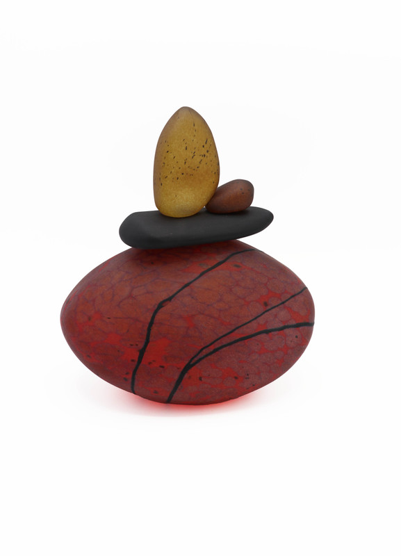 Blown glass cairn sculpture by Melanie Leppla with three glass stones stacked on top of a deep red base