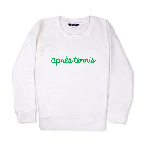 White sweatshirt lays flat on white background with green text reading apres tennis embroidered on the front