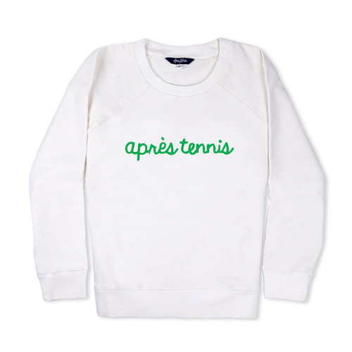 White sweatshirt lays flat on white background with green text reading apres tennis embroidered on the front