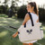 Model walks holding Natural canvas tote with navy straps and front panel embroidered with navy crossed racquets and lime tennis ball.