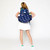 Girl stands wearing navy kids tennis backpack with repeating green heart shaped tennis balls and pink x and o.