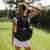 Model in white tennis dress stands on grass tennis court wearing the black tennis backpack