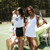 Woman stands on a tennis court with a white sweatshirt with navy crossed racquets embroidered on the front tied around her shoulders
