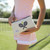 model stands with small natural canvas pouch with navy zipper and navy crossed racquets embroidered on front