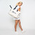 Woman stands on a white background facing the side and smiling. She holds a love all court bag over her shoulder. The canvas tote bag reads love in a cursive font.