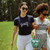 Woman walks with friends on grass. She is wearing a navy t-shirt with the word golf embroidered on the front