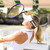 Woman stands on tennis court shading face from sun with tennis racquet. She is wearing a tennis ball overlap head in the game visor. Front of visor is white and sides are navy with white tennis balls printed on the sides.
