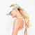 Woman on white background wears olive camo head in the game visor. Front of visor is white and sides are olive camo pattern with white crossed racquets printed over the camo.