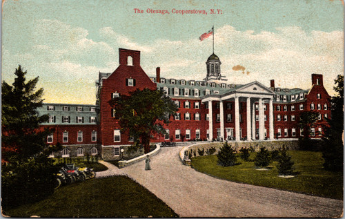 Antique postcard of the Otesaga Hotel in Cooperstown New York showing the red-brick building with white columns and American flag, circa 1912.