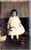 Young girl in white dress and black shoes standing next to plant Velox 1907-1914