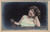 Young girl in green dress resting head on hand leaning against a fence