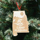 Camp Alabama wooden ornament shaped like Alabama featuring engraved camping scene with tent, campfire, trees, moon, and lake, hanging on Christmas tree.   (Ribbon Color May Vary)