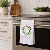 White Christmas flour sack tea towel featuring a watercolor greenery wreath with a red bow and Merry Christmas lettering for festive holiday kitchen décor.