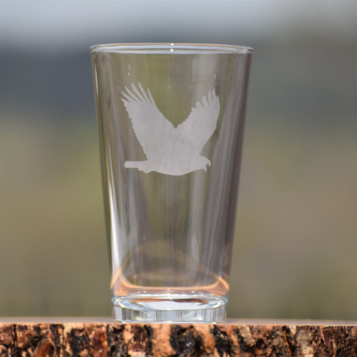 Eagle etched pint glass by Alabama artist Elizabeth Mize, shown filled with beer, highlighting detailed handcrafted eagle design on clear glass