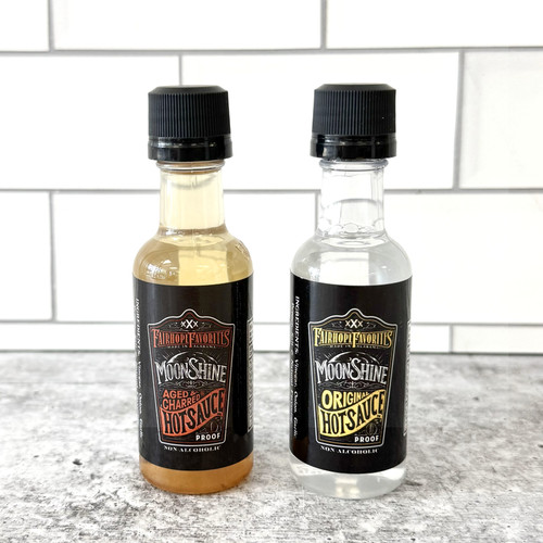 Mini Moonshine Hot Sauce in clear glass bottle, Alabama gourmet hot sauce gift, crystal clear hot sauce close-up, unique Southern hot sauce packaging