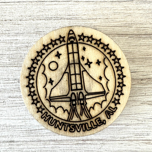 Wooden rocket magnet engraved with Huntsville AL text, natural wood grain visible, round Alabama souvenir magnet on refrigerator surface