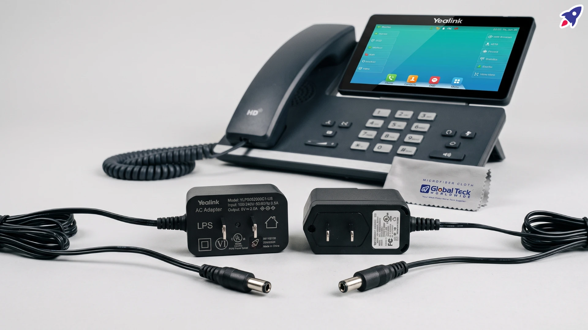 Two black 5V 2A power adapters shown side by side on a light grey surface, one bulkier and one slim, with their barrel connectors facing forward beside a business desk phone.