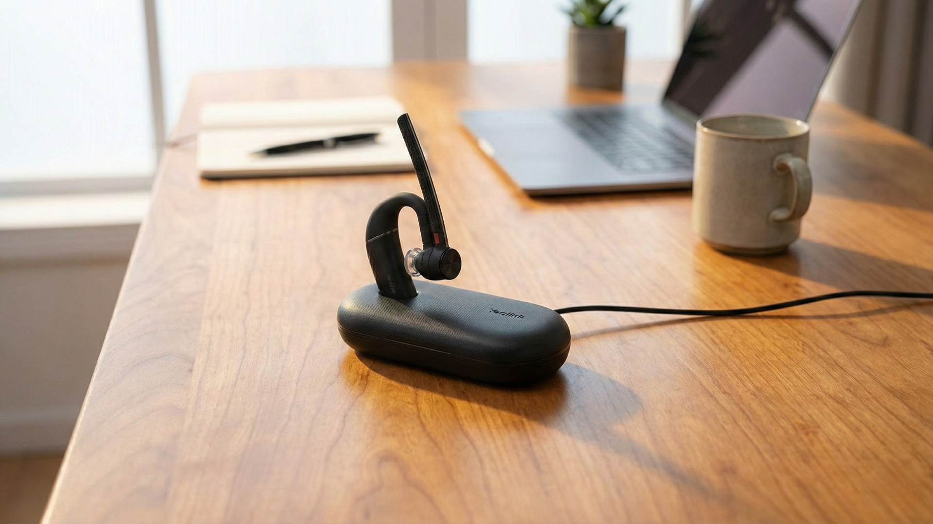 An over-the-ear Yealink BH71 Bluetooth headset charging in its portable charging case.